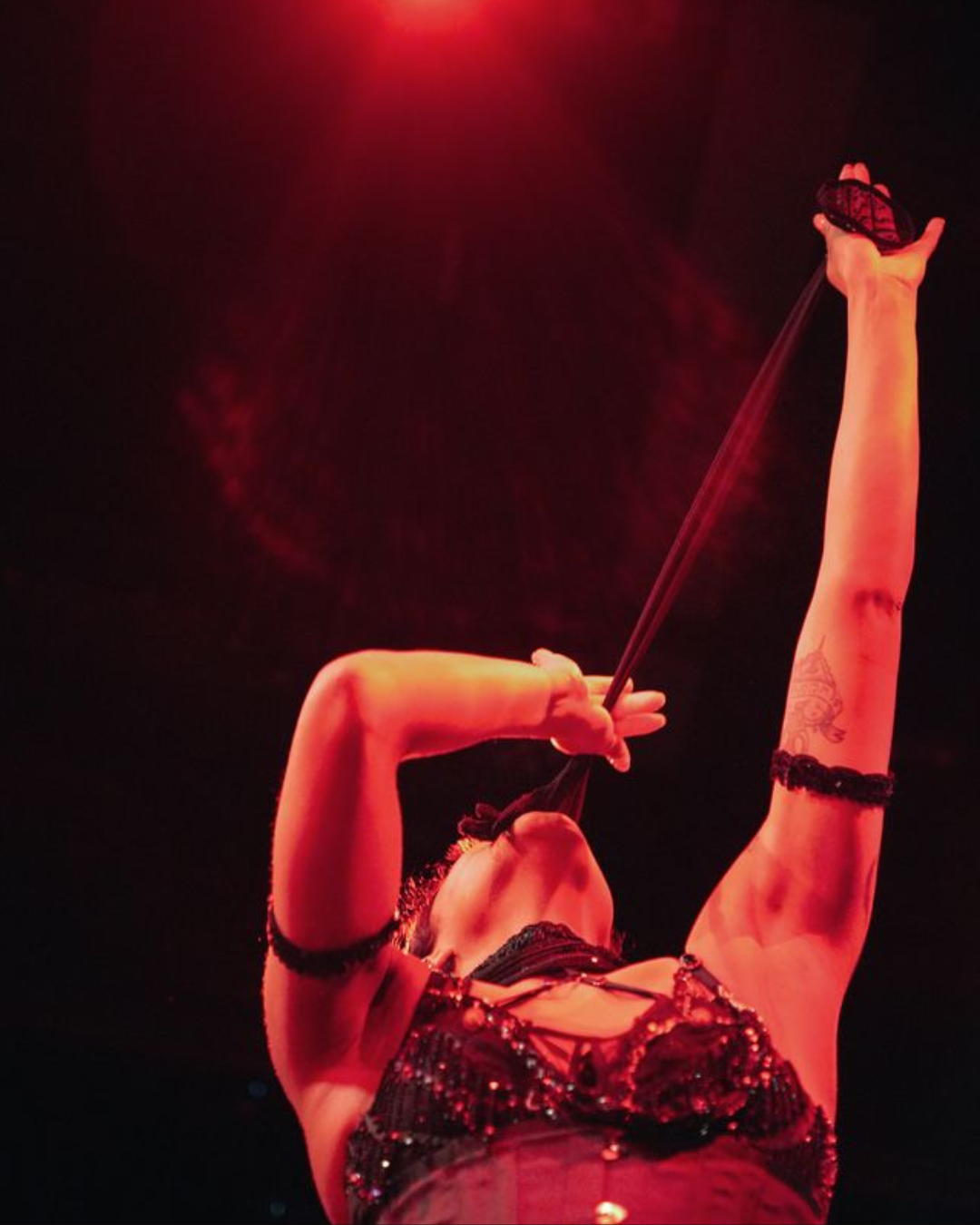 Performer bites a glove and pulls it, stretching it out of their mouth.